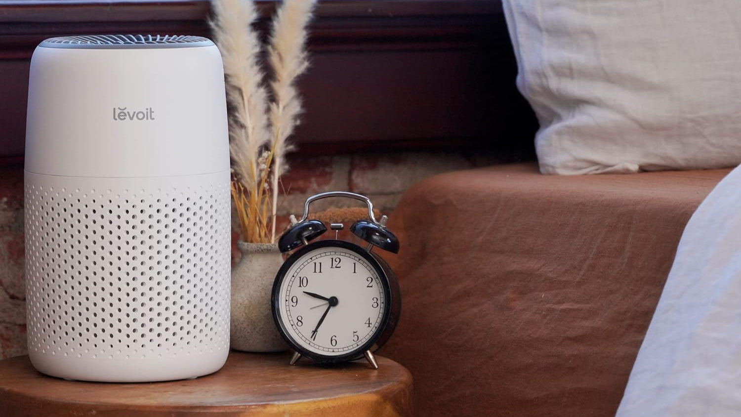 Levoit air purifier on a wooden surface with a clock and decorative plant in the background.